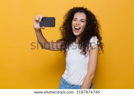 Image of an excited happy cute young woman posing isolated over yellow background take a selfie by mobile phone.