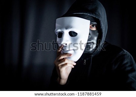 Mystery hoody man wearing black mask holding white mask. Anonymous social masking. Major depressive disorder or bipolar disorder. Halloween concept Royalty-Free Stock Photo #1187881459