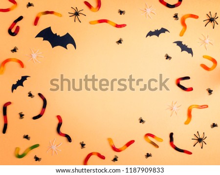 Halloween background with frame of jelly worms, bats and decorative spiders. Space for text.