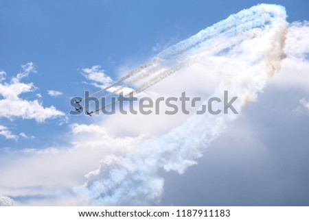Three planes flying through the sky with their rotors and engines on, travelling close to one another and generating white smoke clouds behind them with cloudy summer sky in the background in Poland