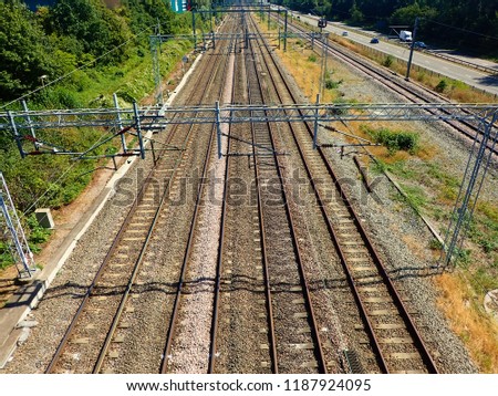 A view of train tracks and power lines from a road bridge.