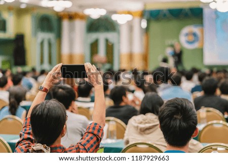 Closeup woman audience hand holding smart mobile phone for taking photo or doing Live streaming to Asian Speaker with casual suit on the stage present the screen in conference hall or seminar meeting