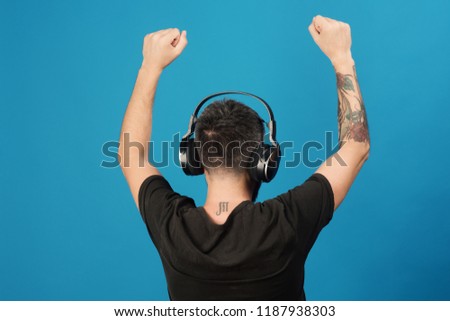 Technologies and music concept. Dj with scorpio tattoo wears headphones, copy space. Singer listens to music partying. Man holds hands up and dances on blue background.