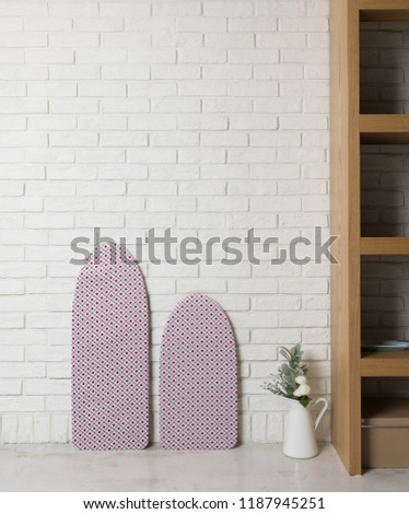 Ironing board with laundry on light background.