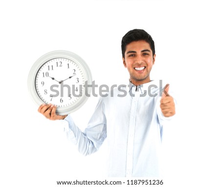 Young man holding a clock while doing a thumb up gesture with his hand against a white background