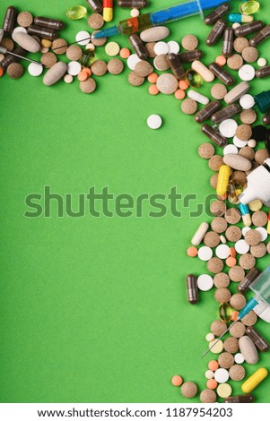 Set of colorful pills scattered on green background, copy space. Drugs near syringes among them. Medicine and treatment concept. Frame made of round pills and capsules put in corner