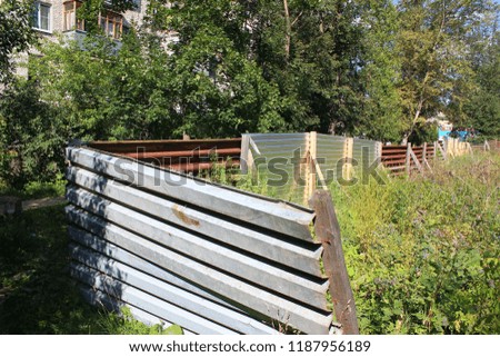 an abandoned construction site that never started, a fenced site for excavation of a construction pit for the Foundation of the building, bent and broken iron fence overgrown with weeds and grass
