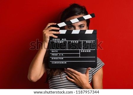 Woman portrait holding movie clapper against colorful red background. Royalty-Free Stock Photo #1187957344