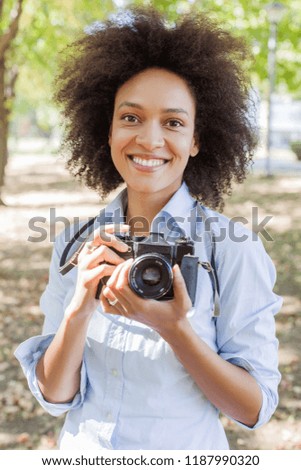 Portrait of charming black woman with retro camera, female photographer outdoor,afro hairstyle, wears casual clothes, looking at camera