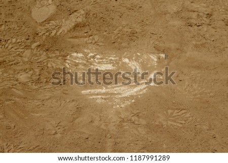 The dirt texture around the dirt covered home plate at the baseball diamond on a sunny day.