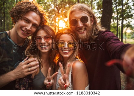 Photo of beautiful hippie people men and women smiling and taking selfie in forest