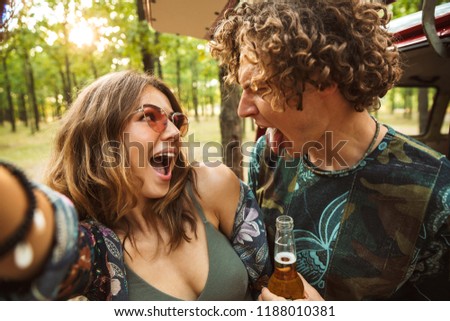 Photo of cheerful hippy couple man and woman smiling and taking selfie in forest near retro minivan