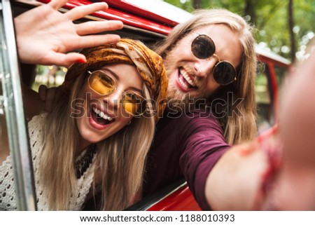 Photo of happy hippie travelers man and woman smiling and sitting in retro minivan in forest