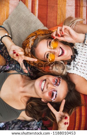 Photo from top of two joyful hippie girls smiling and lying on blanket outdoor head to head