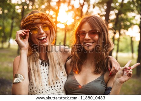 Photo of two happy hippie women smiling and hugging each other while walking in forest