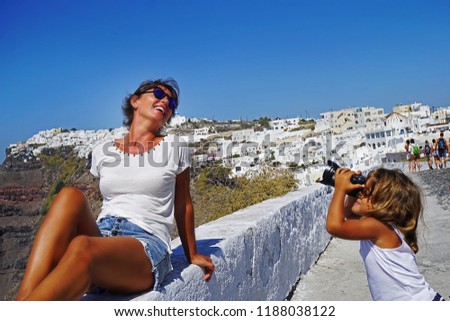 a little girl takes pictures of her mother against the beautiful views of Santorini, Greece