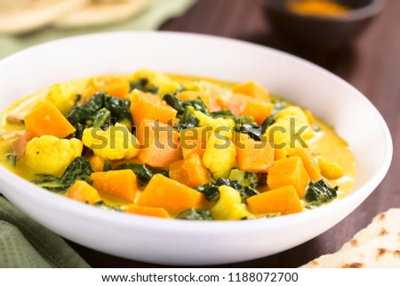 Homemade Indian vegetarian cauliflower pumpkin and spinach curry in bowl, fresh naan bread on the side (Selective Focus, Focus in the middle of the dish) 