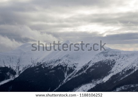 Winter mountain landscape. Wide view of distant woody mountain peaks covered with shiny snow, ice and glaciers under cloudy blue sky on clear cold sunny winter day.