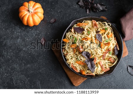 Autumn pasta with pumpkin and bacon in cast iron pan. Homemade spaghetti pumpkin pasta on wooden, copy space. Autumn seasonal food.