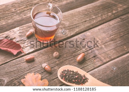 Cup of tea with autumn leaves, acorns and spoonful dry herbal tea on wooden table. Toned photo
