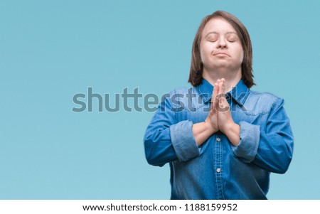 Young adult woman with down syndrome over isolated background praying with hands together asking for forgiveness smiling confident.