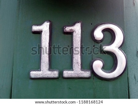 House sign number 113: white digits with black outline against a green painted wooden gate