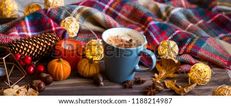 Cup of coffee or hot chocolate with autumn decorations, candle  and a cozy scarf