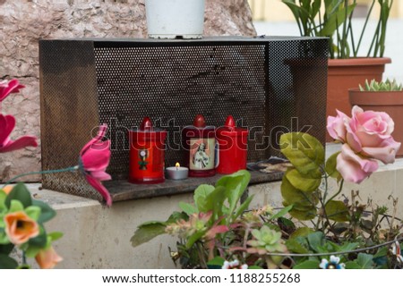 Flowers and Red Candles with a Picture of Jesus on a Wall.