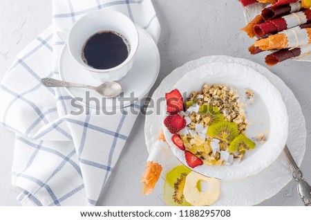 Homemade granola with oat flakes, nuts and dried fruits in a white plate and and pouring coffe in cup on white concrete background, selective focus 