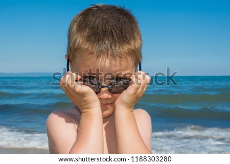 a beautiful little boy posing on a beach by the sea with sunglasses