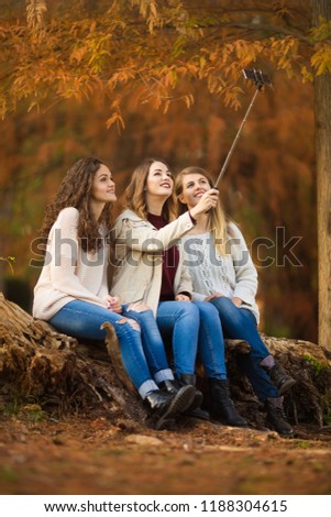 Three young women sitting in the park in autmn and taking selfie