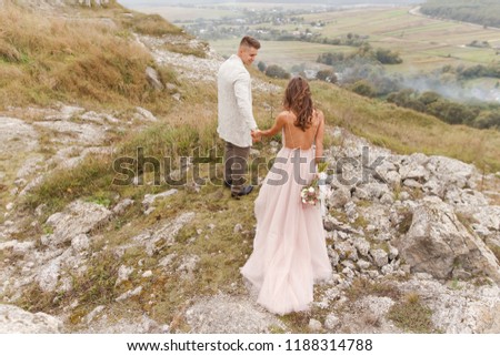 Happy bride and groom in a charming wedding dress with a beautiful bouquet in the mountain near the rocks