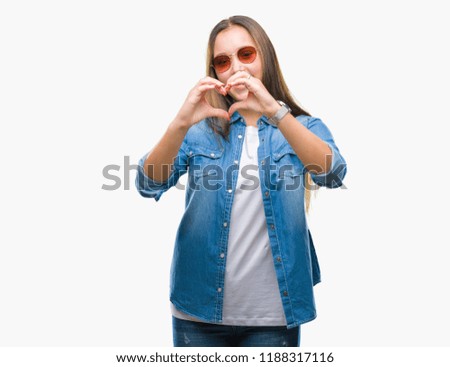 Young beautiful caucasian woman wearing sunglasses over isolated background smiling in love showing heart symbol and shape with hands. Romantic concept.