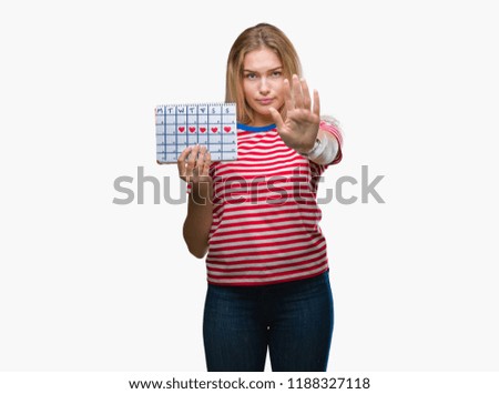 Young caucasian woman holding menstruation calendar over isolated background with open hand doing stop sign with serious and confident expression, defense gesture
