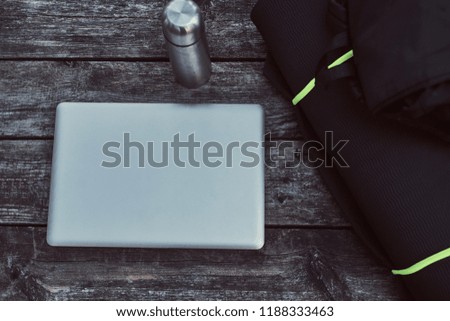 Close-up photo of a laptop, smartphone and thermos bottle on wooden table outdoors.