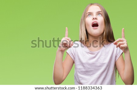 Young beautiful girl over isolated background amazed and surprised looking up and pointing with fingers and raised arms.