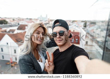 Funny beautiful young couple doing selfie. Handsome man with sunglasses shows a sign of peace with a beautiful girl traveling in the city