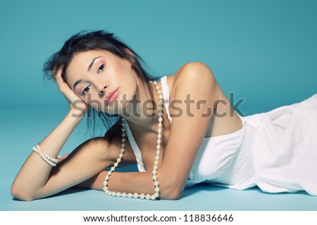 beautiful girl in white dress lying and beads over blue background