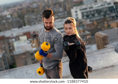 Young couple working out on a building rooftop terrace, lifting weights, doing arms exercises. Focus on the woman