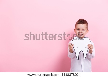 A little boy with a papercraft tooth on a pink background. Healthcare concept