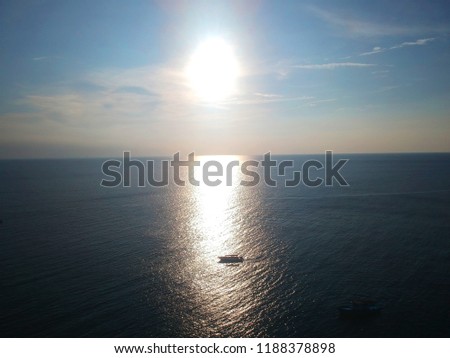 Aerial photo of the sun setting at the horizon while a silhouette of a boat passes by the ray reflected of the sea. Picture taken using a drone.