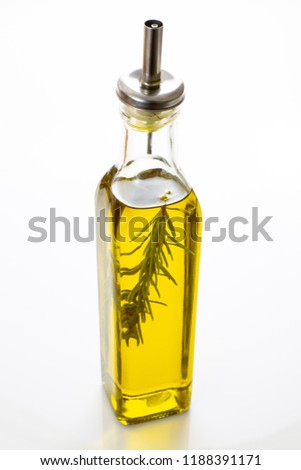 A glass bottle filled with high quality olive oil with a stem of rosemary inside on a kitchen counter waiting for a chef to use it.