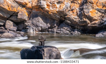 An inukshuk, standing on a rock, is dwarfed by the base of a huge cliff, as the York River rushes over the Egan Chute near Bancroft, Ontario, Canada.