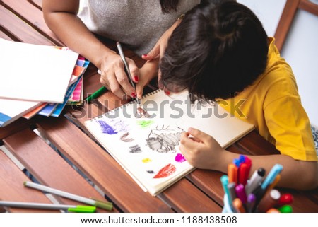 Children homework. Young mixed race boy doing homework in terrace at home with his mother teaching him. Drawing coloring. Focus mood, close up. Back to school concept.