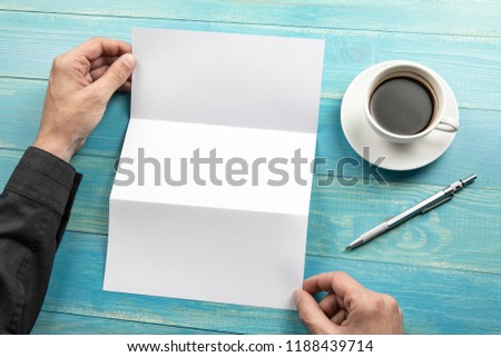 Mens hands holding empty white booklet on blue wooden background. View from above