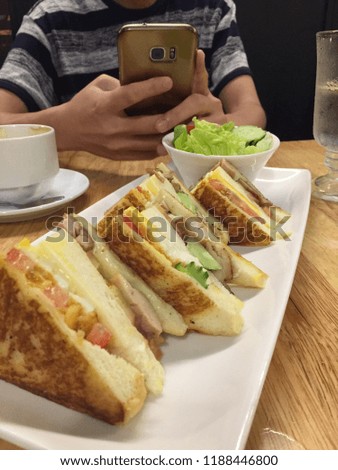 man take picture of sandwiches by mobile phone before eating at restaurant