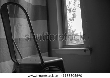 A black and white photograph of an empty chair looking out a window. The theme of this photo is that of mental illness and how one can feel alone and empty making the "outside" look narrow and focal.