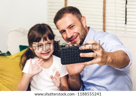 Father with little daughter having fun and taking selfie together with smartphone while sitting on the sofa at home.Love of family and concept