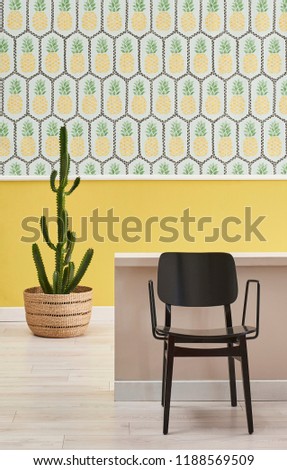 Pineapple wallpaper and yellow background in the room. Brown stand and home accessory. Laptop technological tool in the room. Decorative home style.