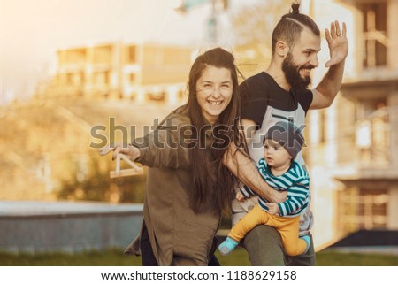 Happy young family. Stylish bearded man and young beautiful wife with a little child in their arms, hugging, kissing and playing walking around the autumn city.